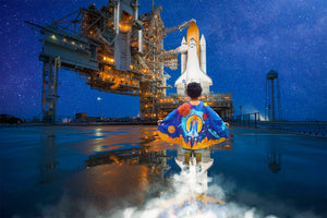 Young boy with a superhero cape standing in front of a space shuttle launch