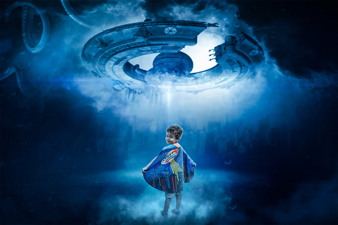 Young boy wearing a superhero cape and standing below a spaceship